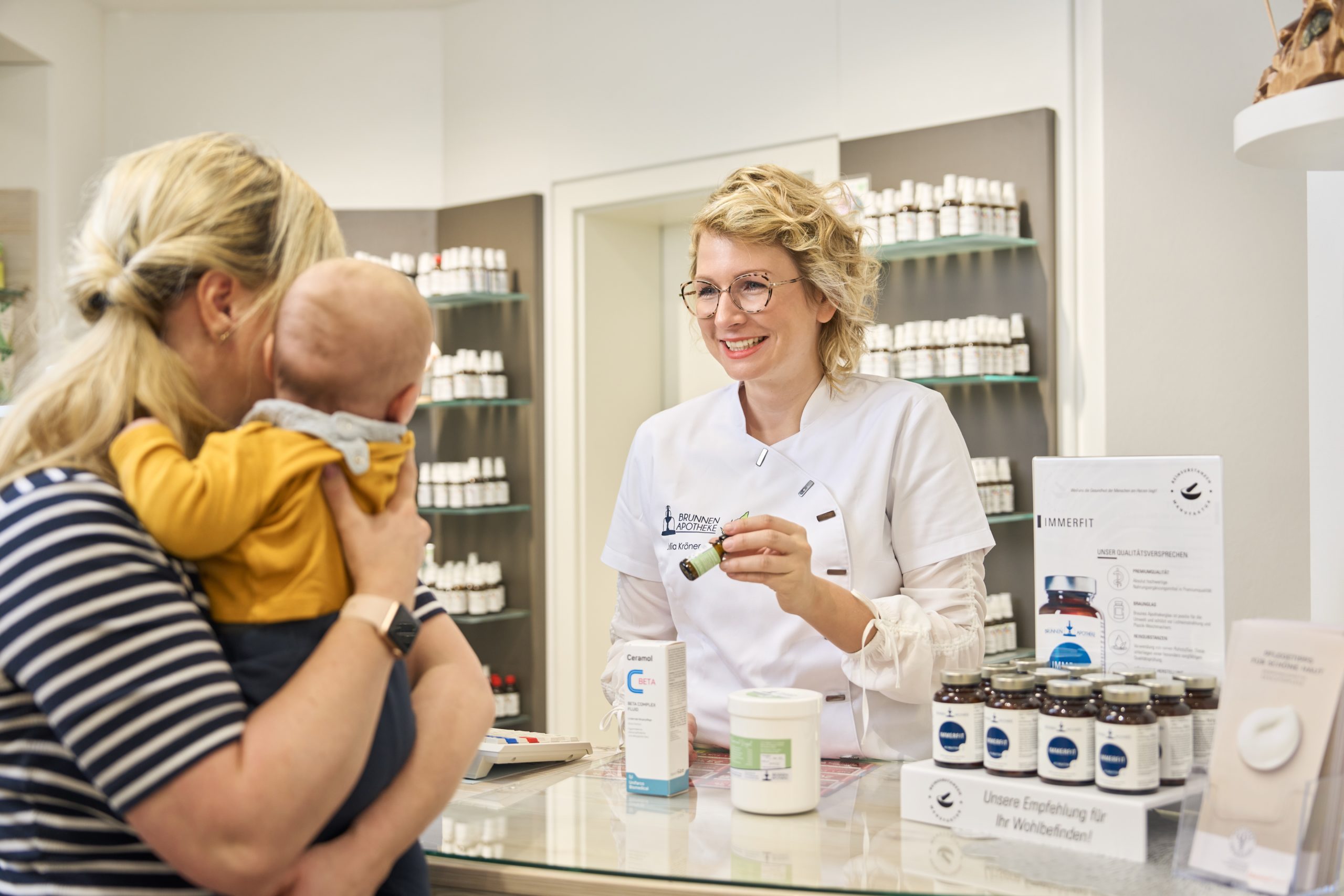 Apothekenleiterin Julia Kröner berät Mutter mit Baby und zeigt verschiedene Medikamente